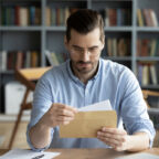 Serious,Businessman,Sit,At,Workplace,Office,Desk,Holding,Envelope,Take