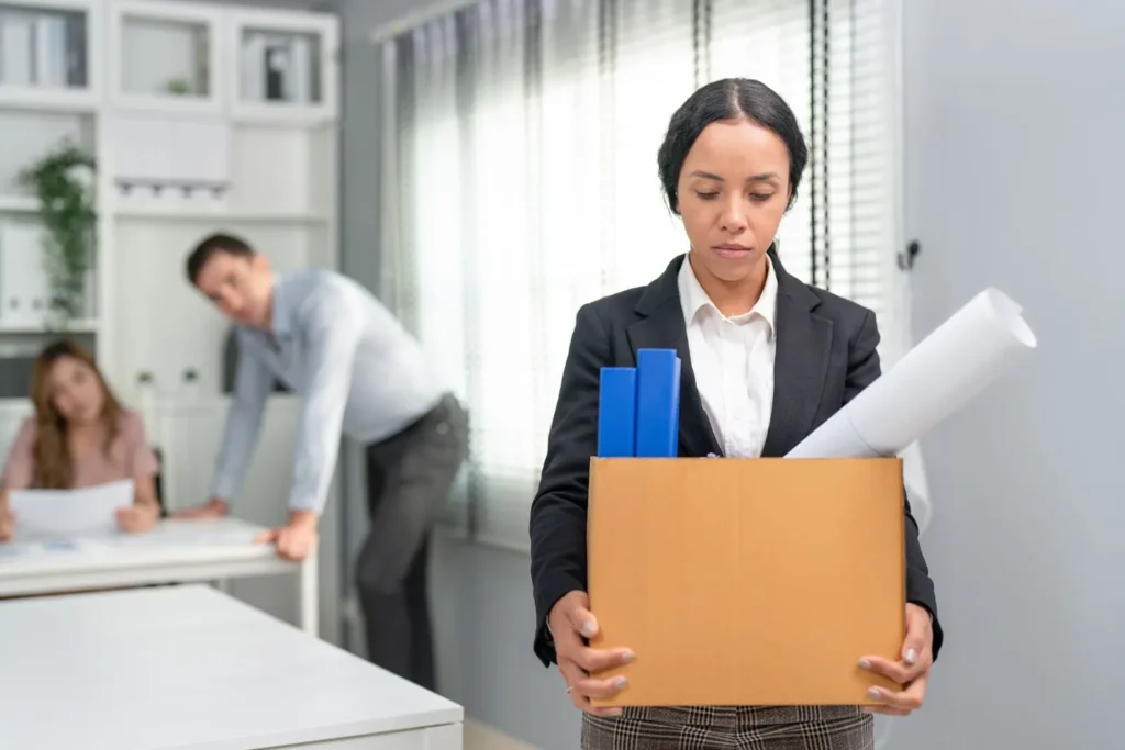 A woman is leaving her workplace, holding a box with her belongings.