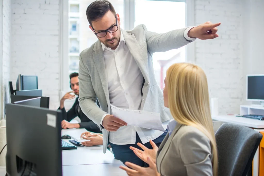 A man in an office, angrily pointing in a direction with his hand.