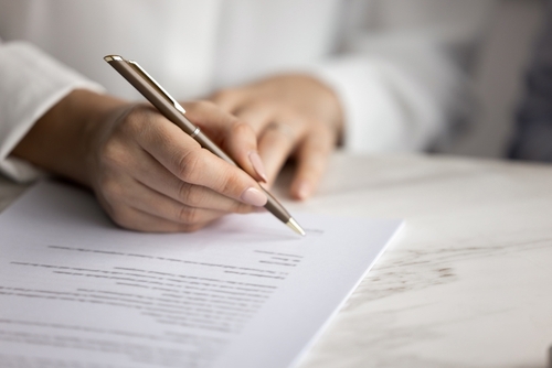 Person signing contract document with pen in close-up cropped shot