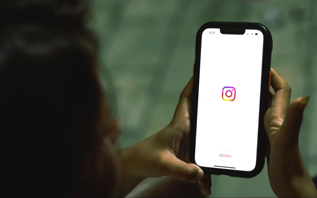 A person holding a smartphone displaying the Instagram application loading screen.