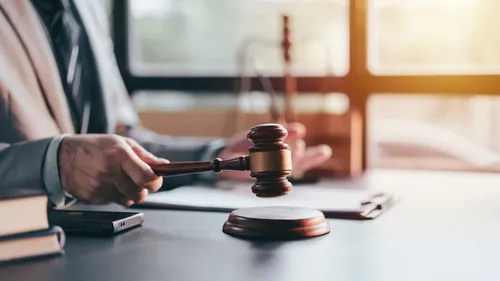 suited attorney striking wooden gavel on sound block at desk with scales of justice